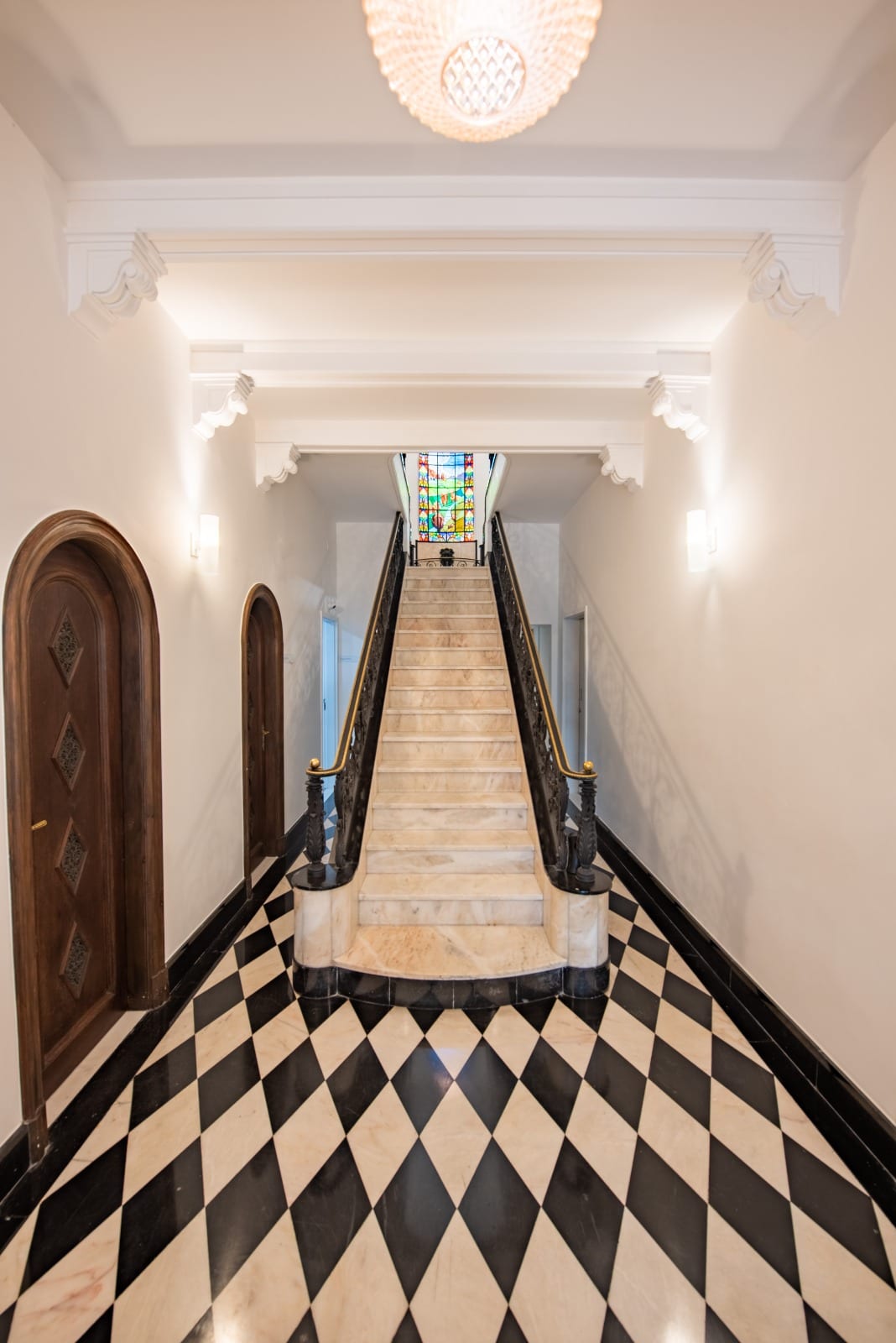 Hall de entrada do casarão da Fonte Imagem, com piso xadrez de mármore, escada de mármore com corrimão de ferro e vitral colorido ao fundo