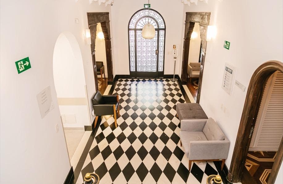 Hall de entrada da Fonte Imagem com piso xadrez preto e branco e porta com vitral